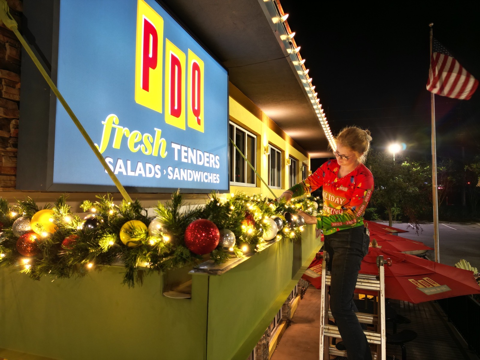Lipham Lighting crew member on a ladder installing lit garland and ornaments under the PDQ sign
