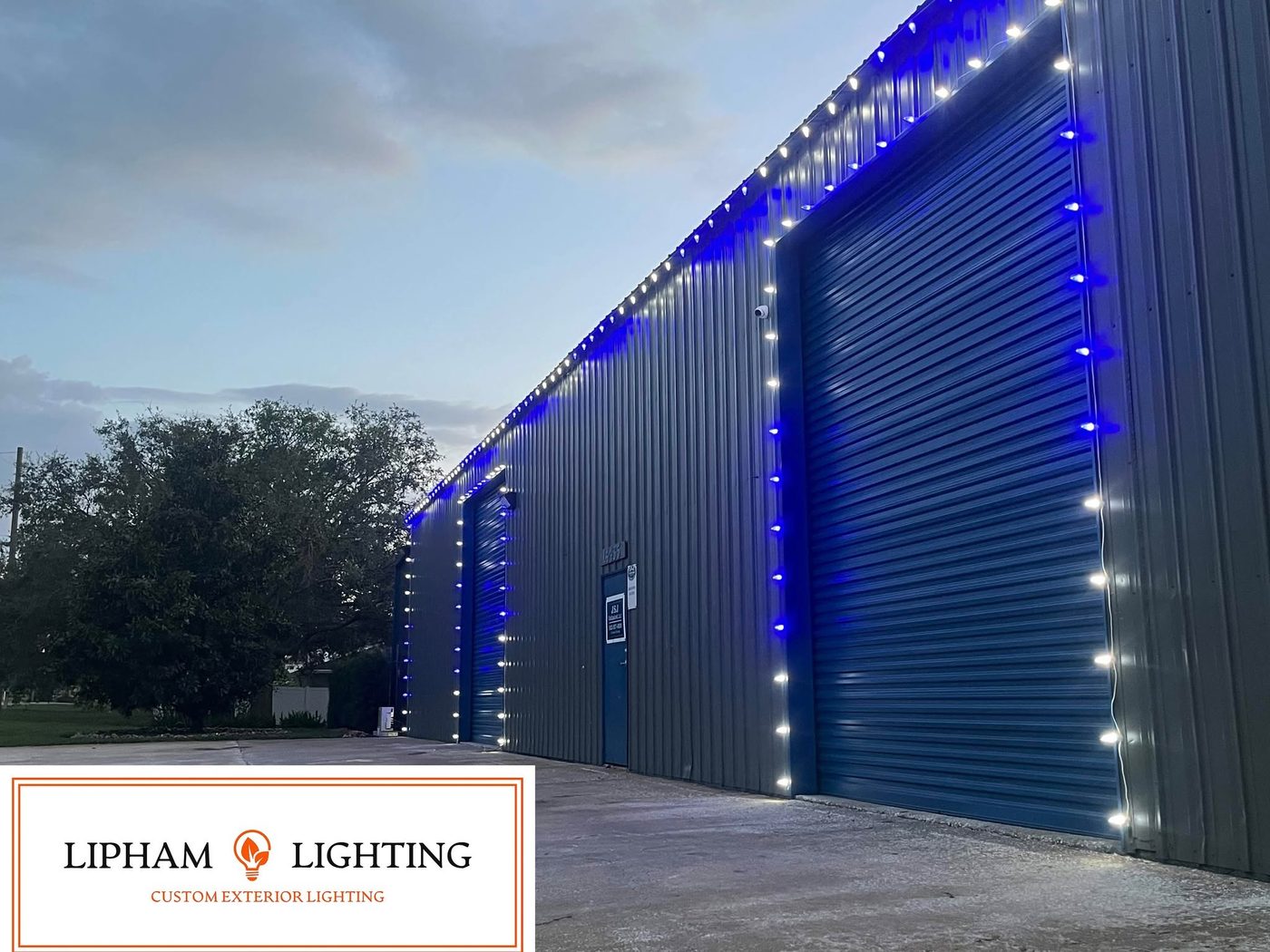 Industrial warehouse with blue and white holiday lights outlining the roofline and bay doors