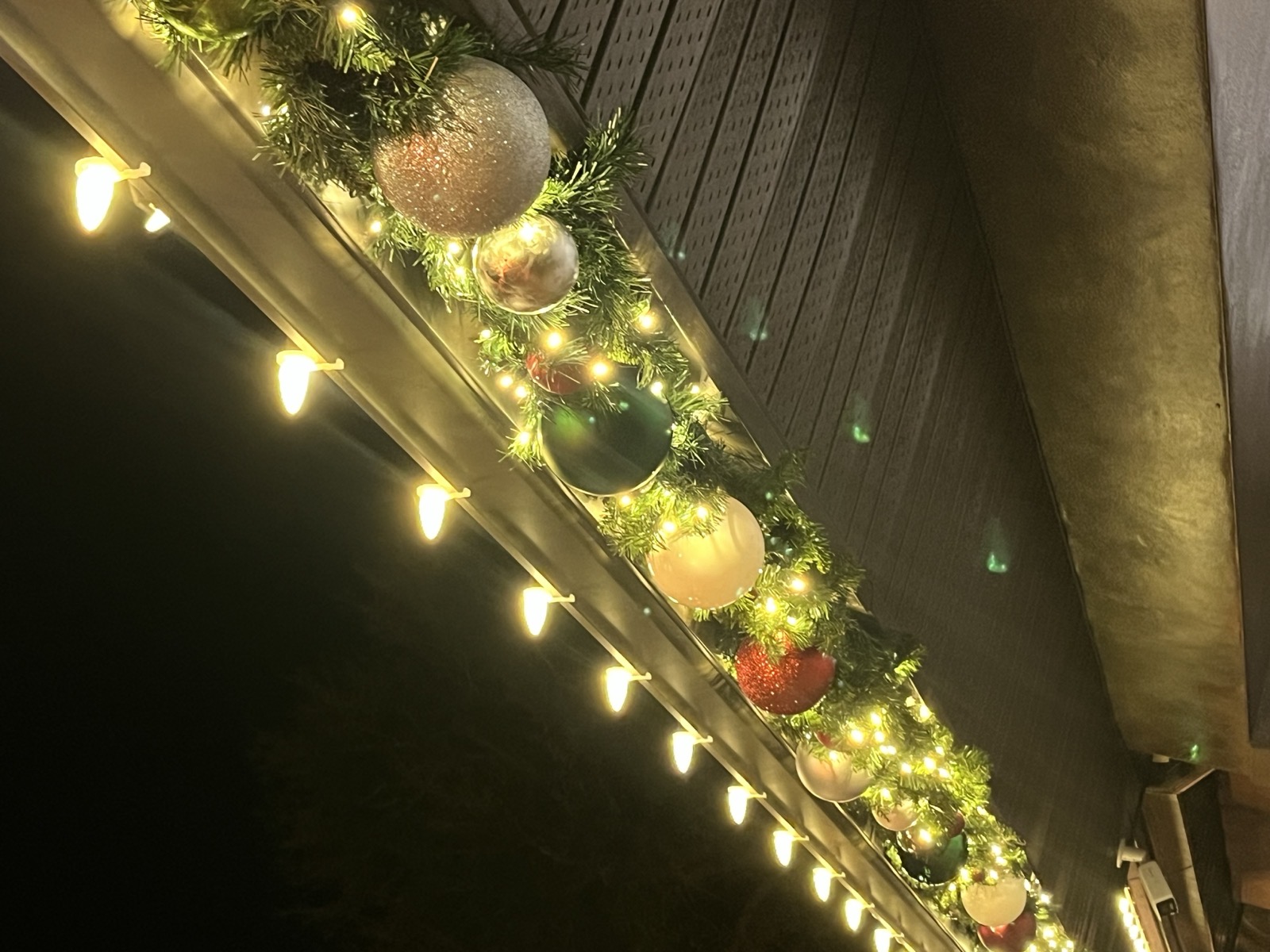 Close-up of lit garland with oversized ornaments along a home eave