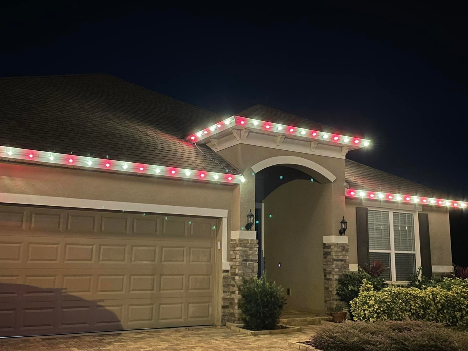 Red and white holiday lighting tracing an arched stone entryway at night