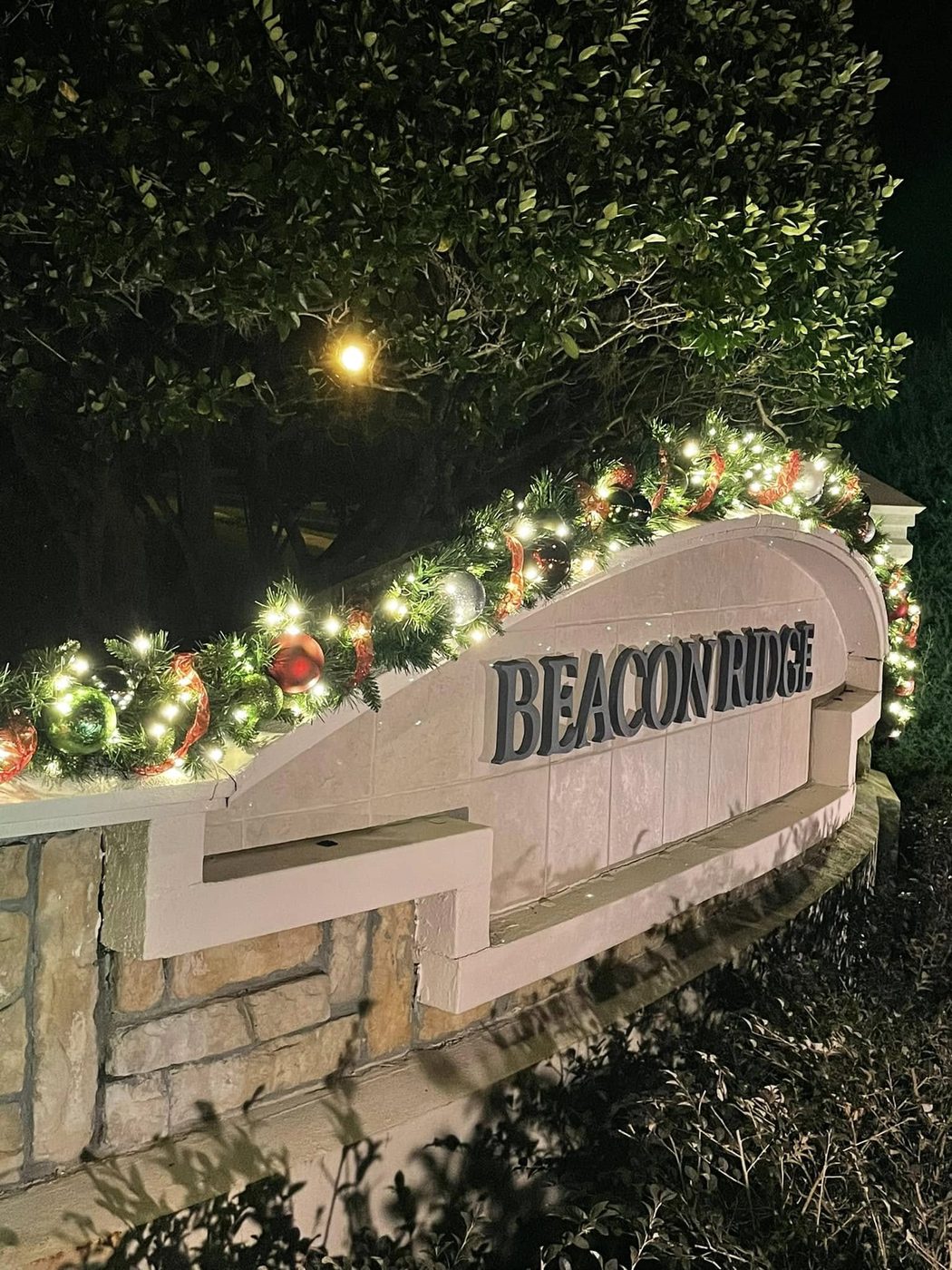 Beacon Ridge monument sign topped with lit holiday garland, ornaments, and red ribbon