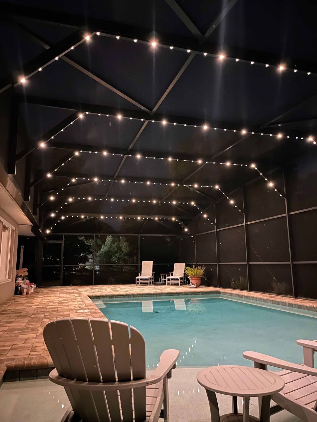 Screened pool enclosure with permanent warm white lighting tracing the cage frame at night