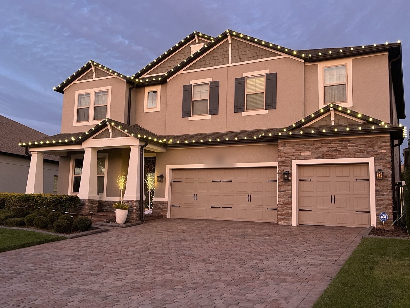 Two-story home with warm white roofline lighting along every peak at dusk